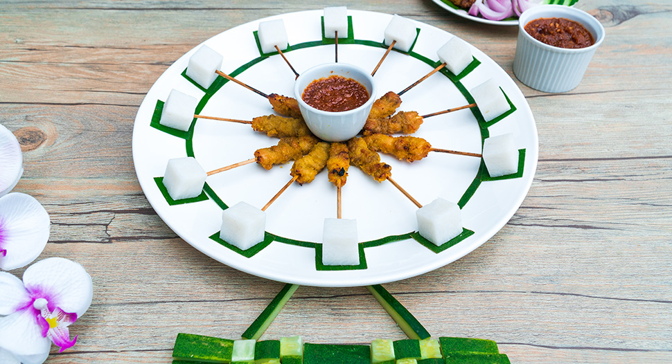 A white plate with sticks of chicken satay and lontong cubes arranged to form the shape of the Singapore Flyer