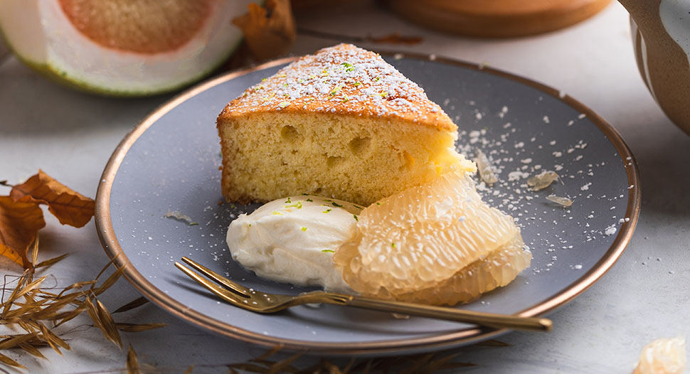 a slice of pomelo cake dusted with icing sugar and served with fresh pomelo and whipped cream