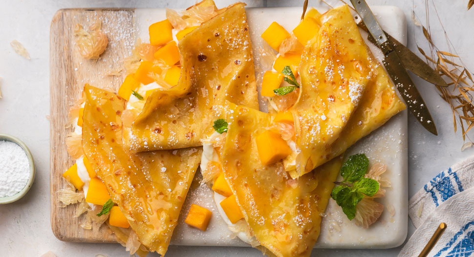Sweet pomelo and mango cubes between fluffy layers of crepe served on a board
