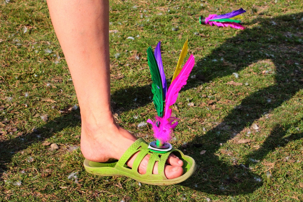 A person's foot balancing a colourful feathered shuttlecock