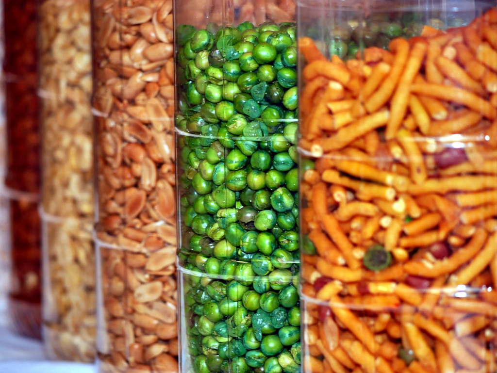 A row of large transparent containers, each filled with peanuts, dried green peas and other assorted kacang puteh nuts