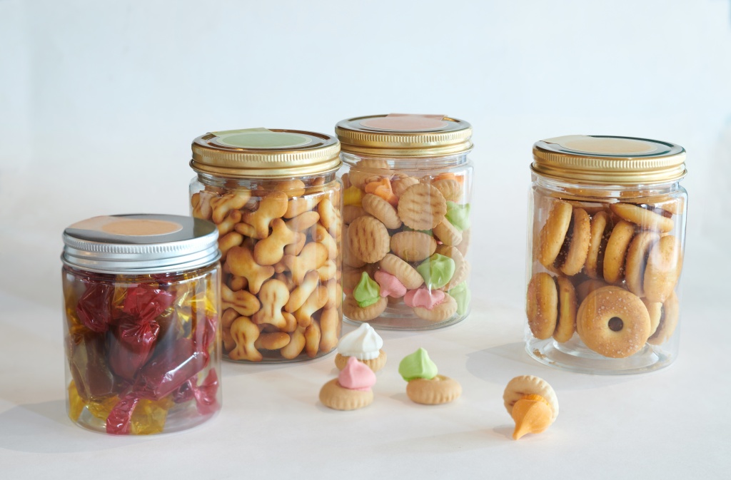 Four transparent containers with golden lids, full of old-school biscuits like fish crackers and iced gem biscuits